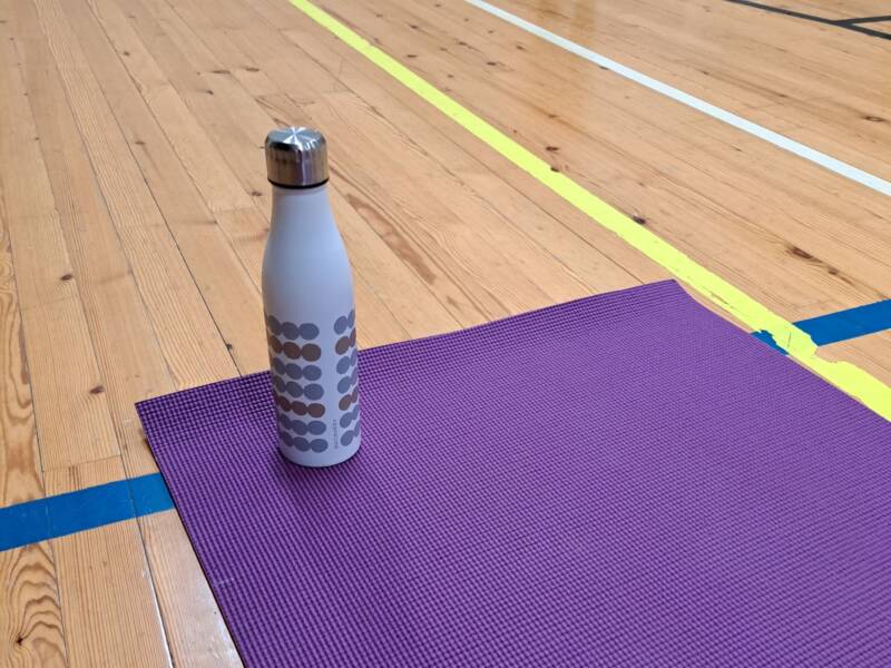 Liikuntasalin lattialla violetti jumppamatto ja valkoinen juomapullo.