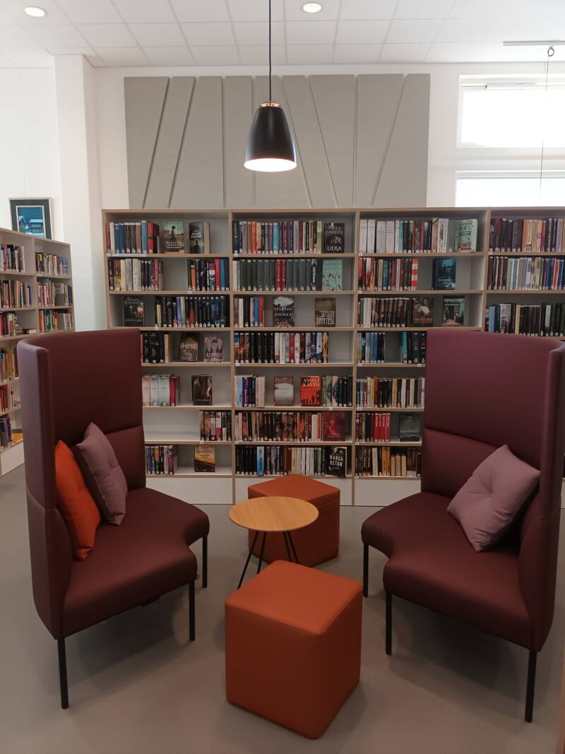Kirjaston oleskelualuetta. Kaksi sohvaa, sohvapöytä sekä kaksi rahia. Taustalla kirjahylly.
