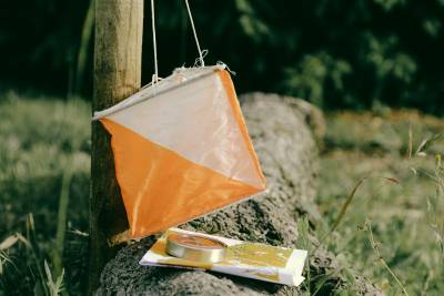 suunnistusrastin merkki roikkuu tolpasta, kivellä kartta ja kompassi